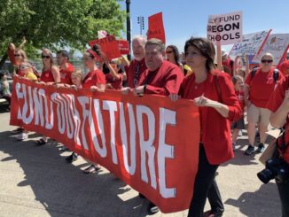 Photo of teachers at a union demonstration, all wearing red union shirts and carrying a banner.