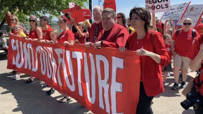 Photo of teachers at a union demonstration, all wearing red union shirts and carrying a banner.