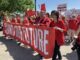 Photo of teachers at a union demonstration, all wearing red union shirts and carrying a banner.