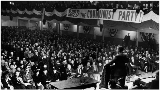 Black and white photograph of a full auditorium from the rostrum; a sign reads BUILD THE COMMUNIST PARTY!