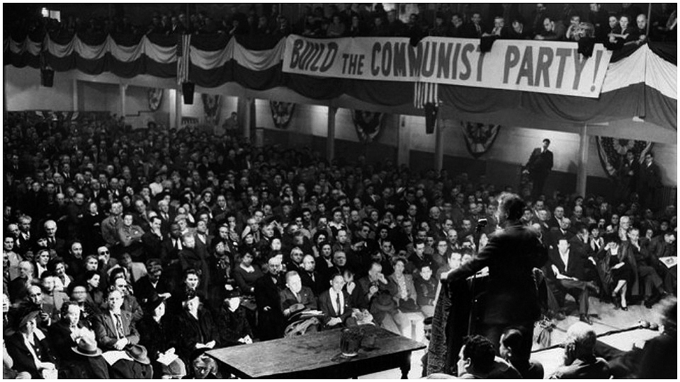 Black and white photograph of a full auditorium from the rostrum; a sign reads BUILD THE COMMUNIST PARTY!