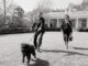 Black and white photo of Ronald Reagan being pulled across the White House lawn by a leashed dog while standing next to Nancy Reagan