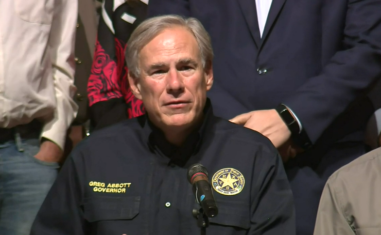 Greg Abbott at a microphone wearing a police-style jacket with a star on the breast